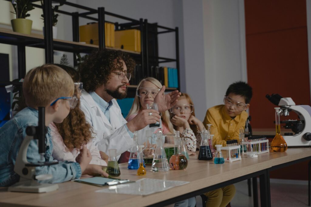 Teacher conducts a chemistry experiment using laboratory equipment in a classroom setting with students.